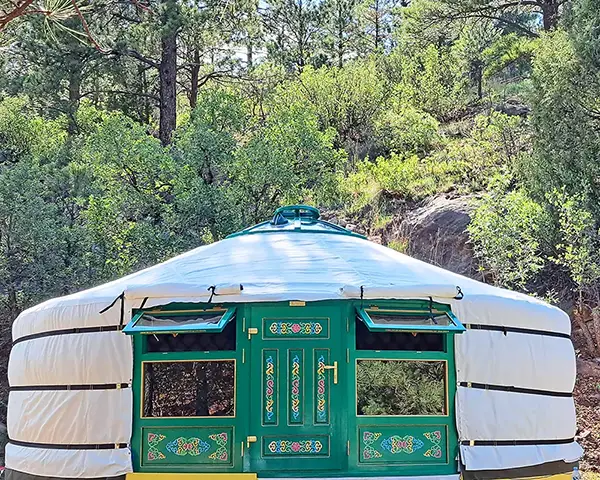 Mongolian yurt with two front windows in green color with trees in the background