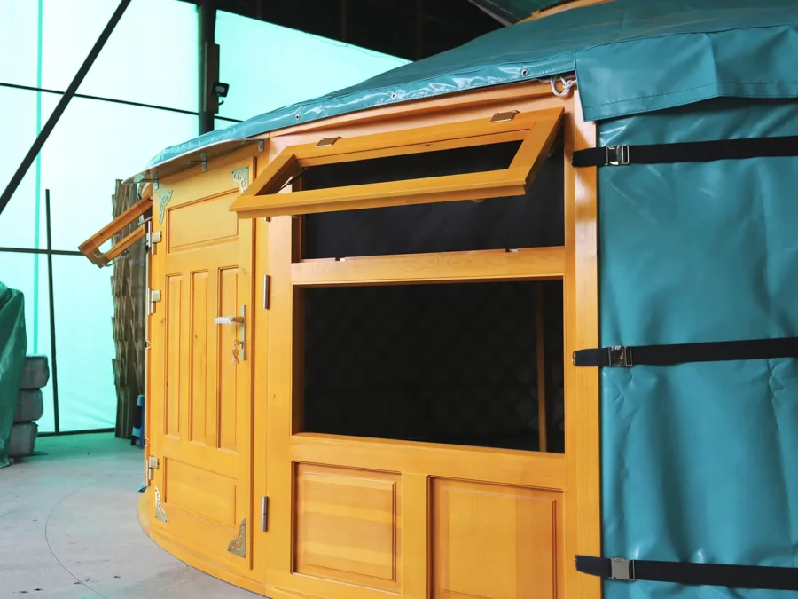 A Mongolian yurt in green cover, with wood windows and door painted in yellow